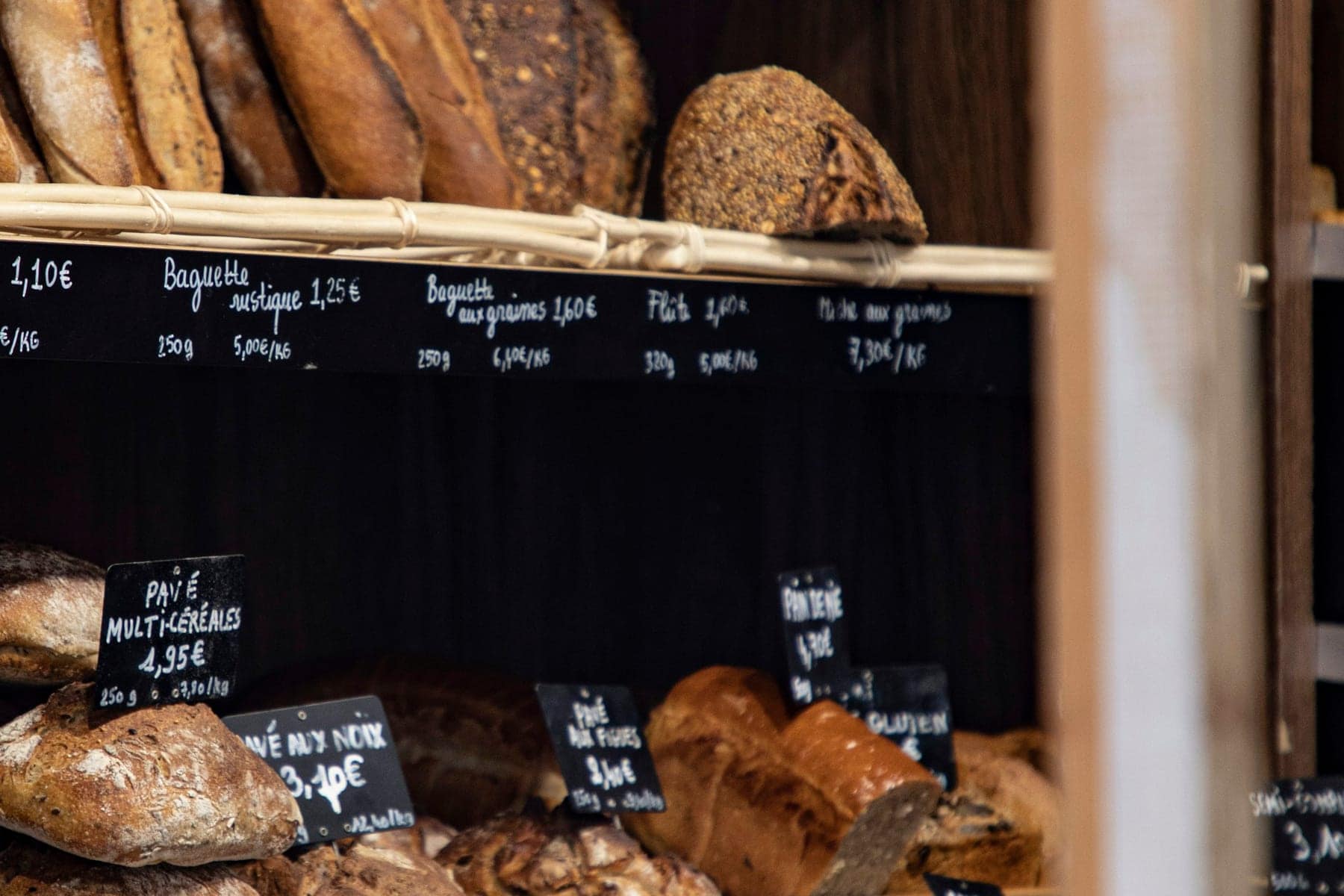 Rayons de pains d'une boulangerie avec ardoises manuscrites indiquant les prix au kilo et à la pièce