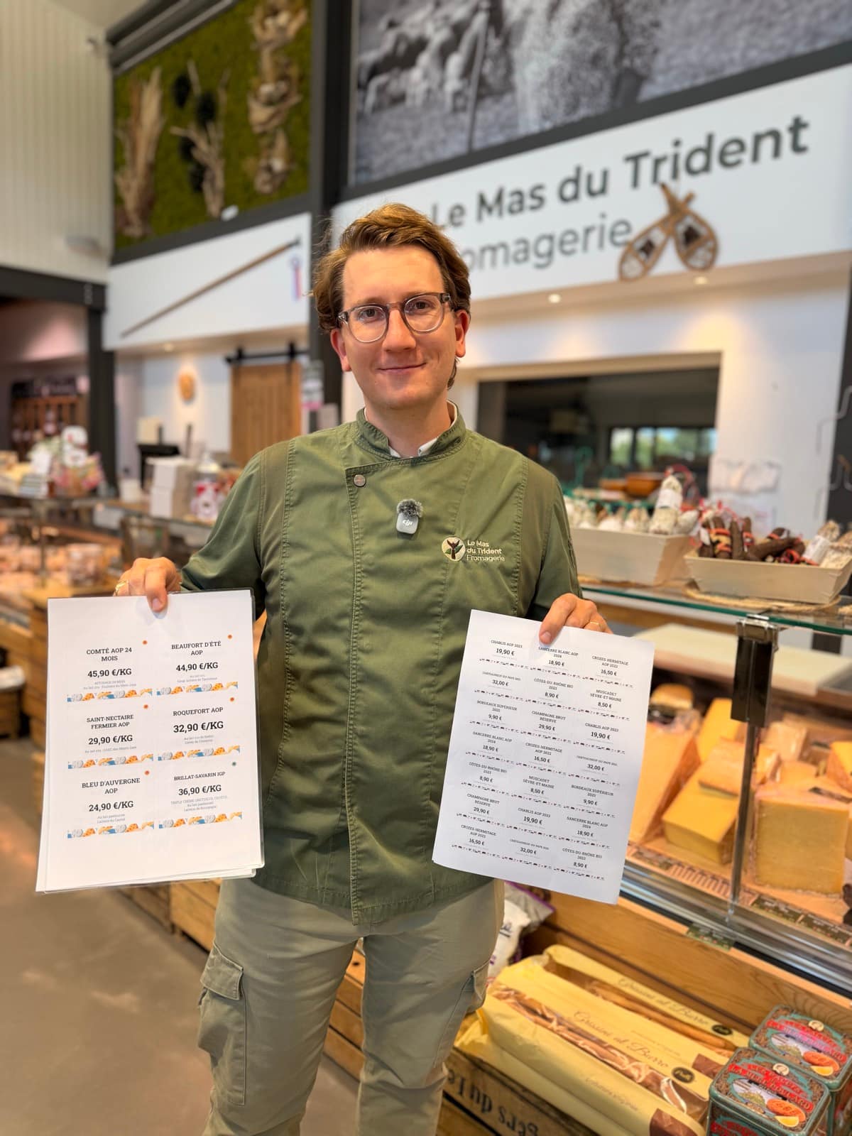 Louis tenant deux planches d'étiquettes de prix imprimées sous l'enseigne Le Mas du Trident