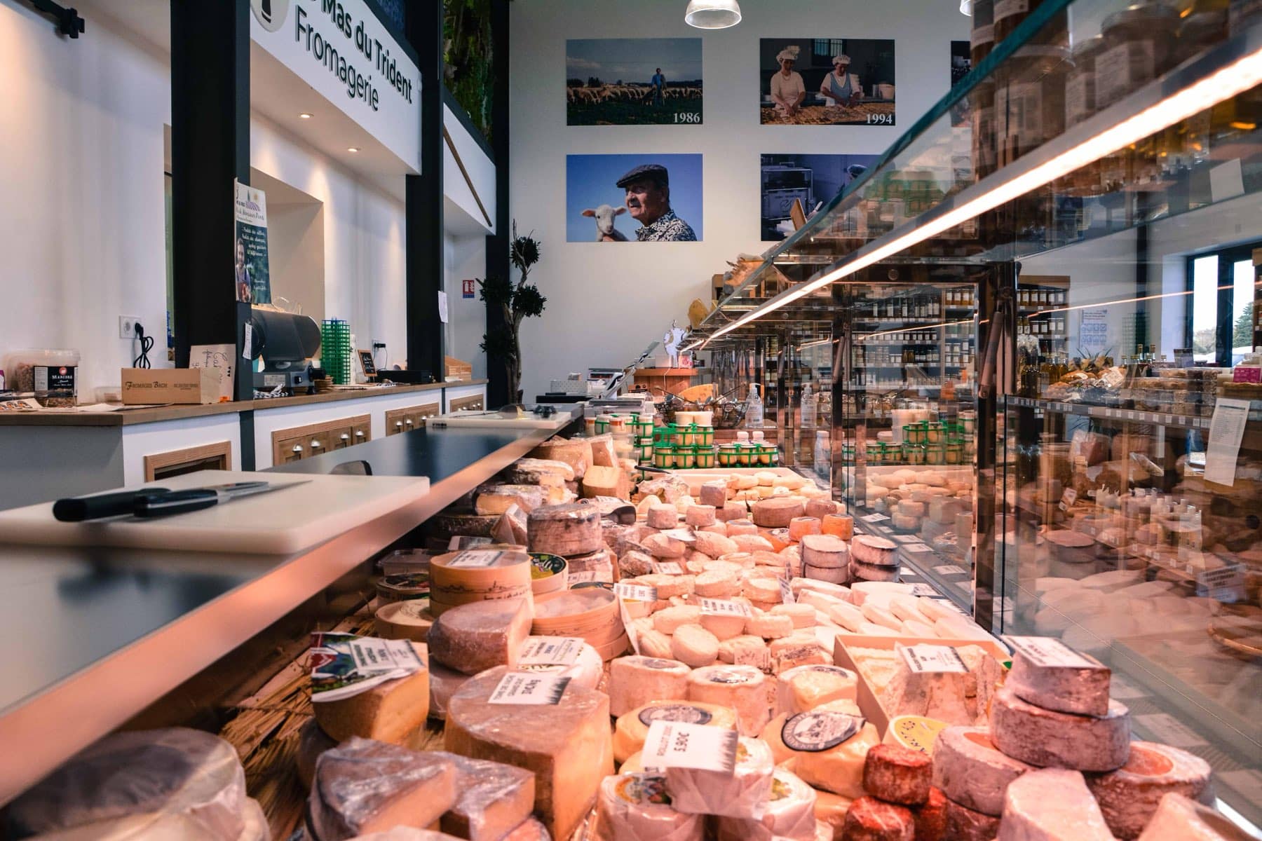 La banque de coupe de notre boutique de Vauvert vue de derrière le comptoir, fromages étiquetés en vitrine et photos de famille au mur