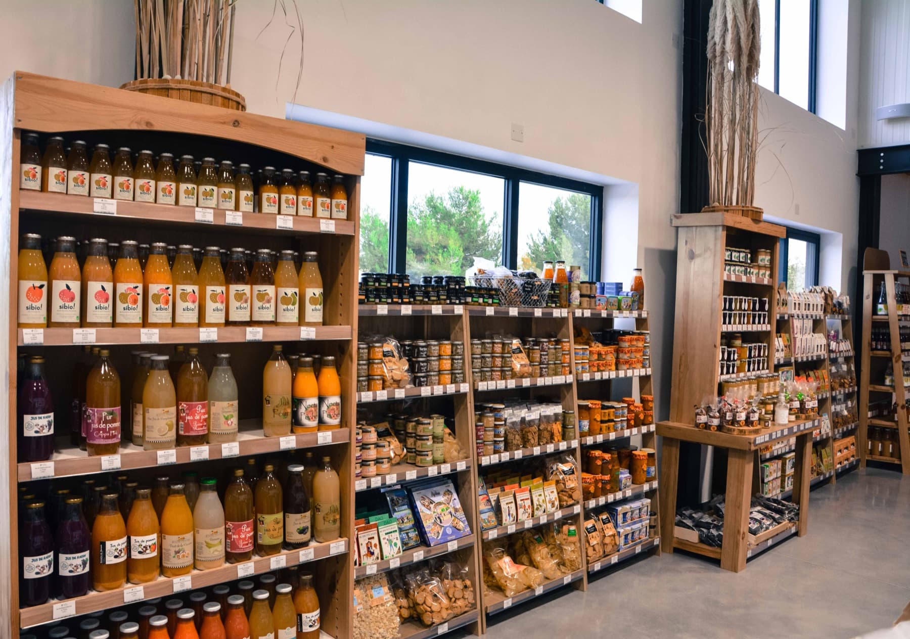 Les rayons d'épicerie fine de la boutique du Mas du Trident à Vauvert : jus de fruits artisanaux, conserves, confitures et biscuits, chaque référence avec son étiquette de prix en rayon