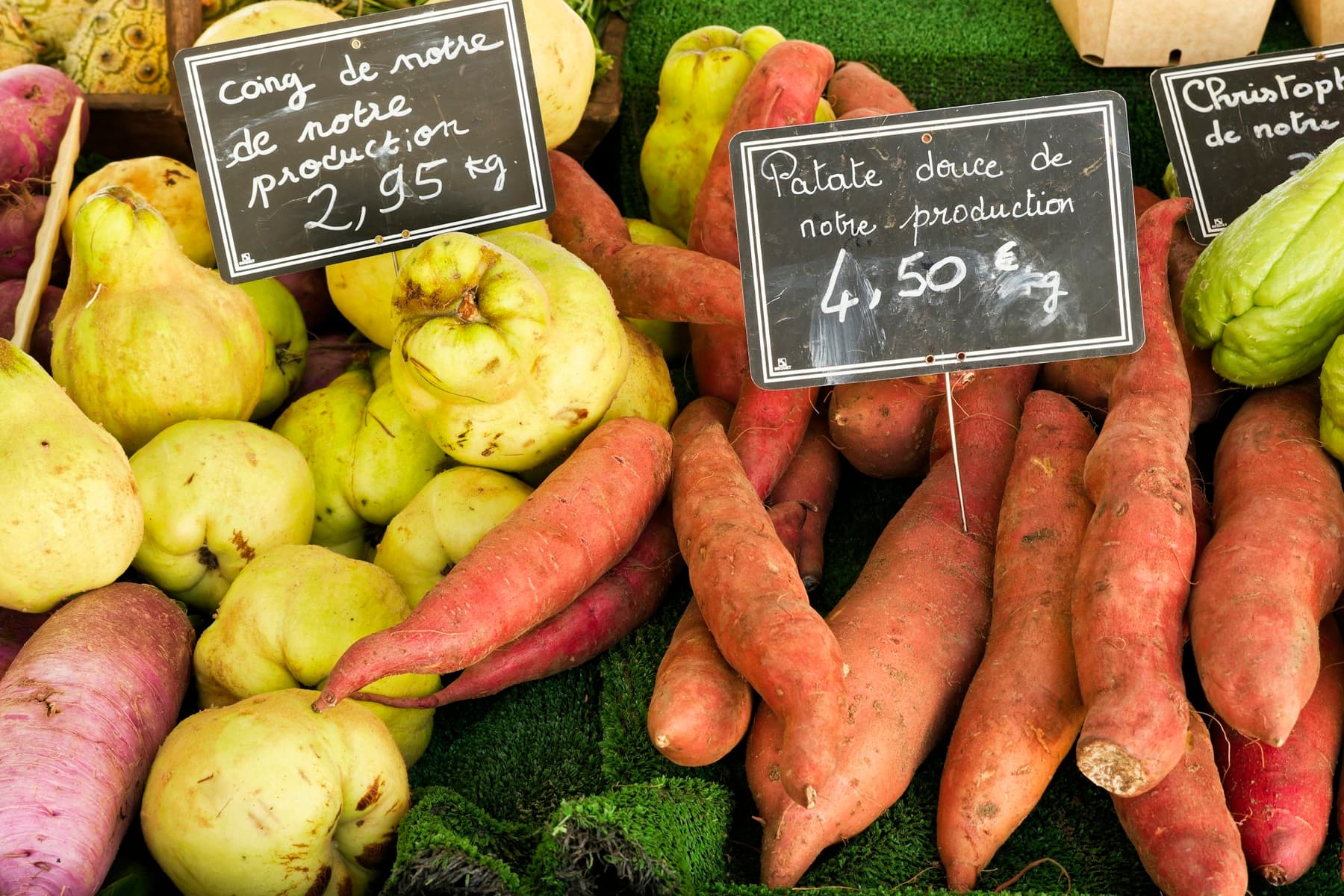 Étal de primeur garni de coings, patates douces, navets et christophines, avec des écriteaux ardoise indiquant les prix au kilo « de notre production »
